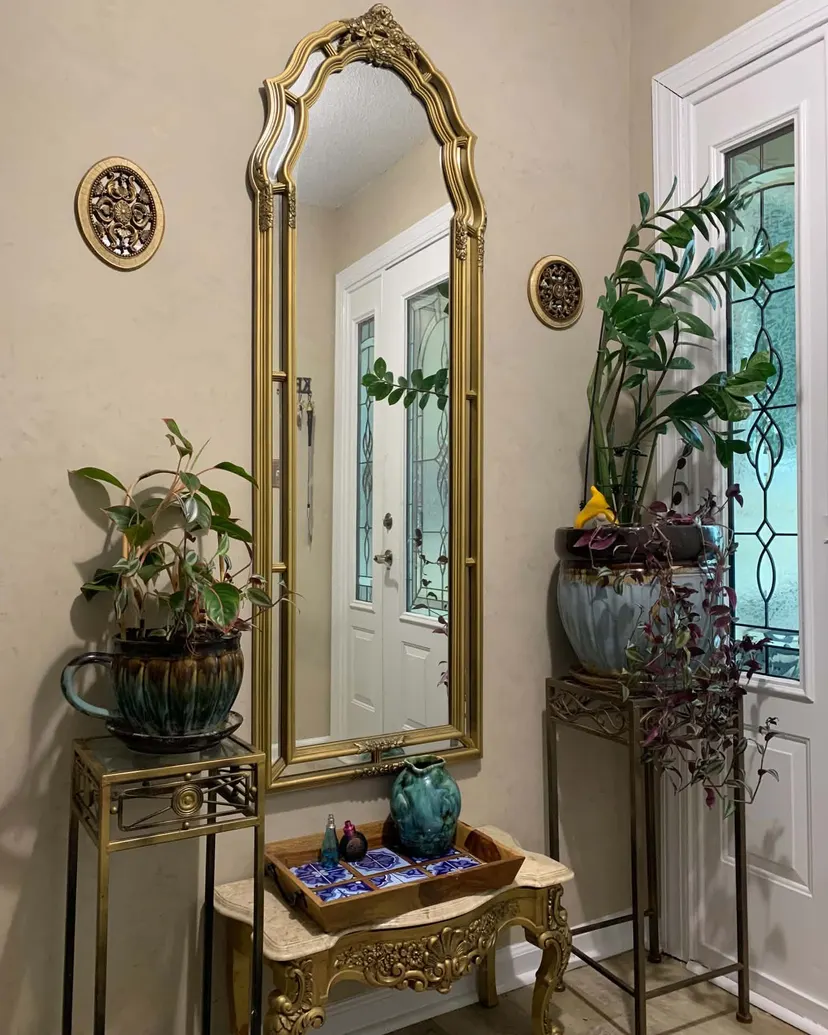 Warm mushroom Roman clay walls around a tall gold arched mirror between two plant stands, beside the front door, in a Carmel foyer