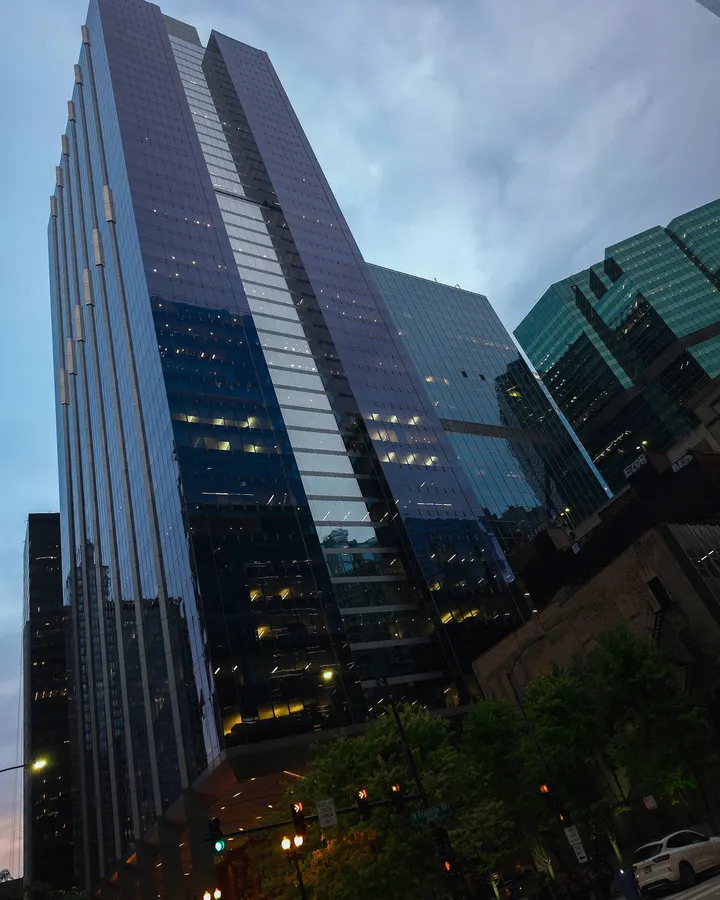Glass towers near Wolf Point in Chicago at dusk, in deep violet, steel blue, and green glass, above trees and an old brick building, a few windows lit