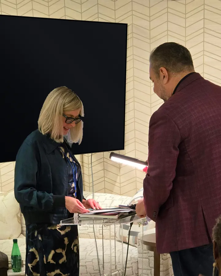 Greg Klopper showing a visitor the colors of The Turn across a clear acrylic table, a chevron-papered wall behind them