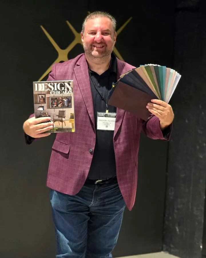 Greg Klopper smiling in a burgundy jacket, holding a copy of Design Chicago and a fan of The Turn’s colors before a dark wall