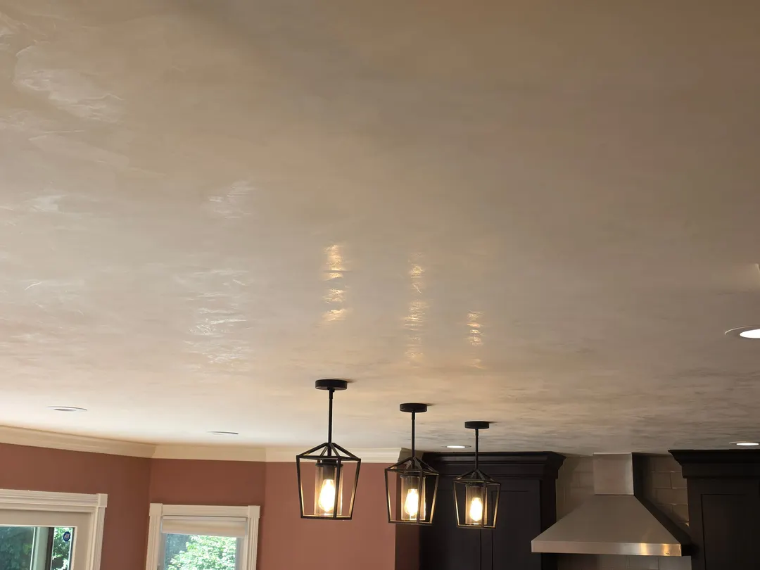 A kitchen ceiling in bone Marmorino lime plaster above terracotta walls and three lantern pendants, in a Geist home
