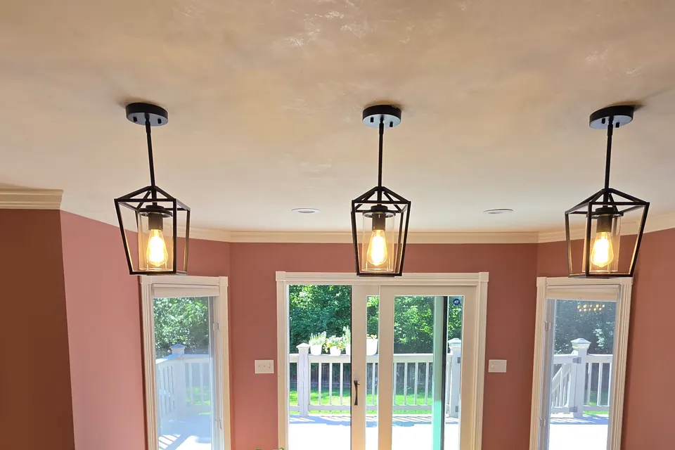The kitchen’s bay of windows and its glass door to the deck, framed in white trim on dusty rose and terracotta walls, under the bone Marmorino ceiling and three lantern pendants