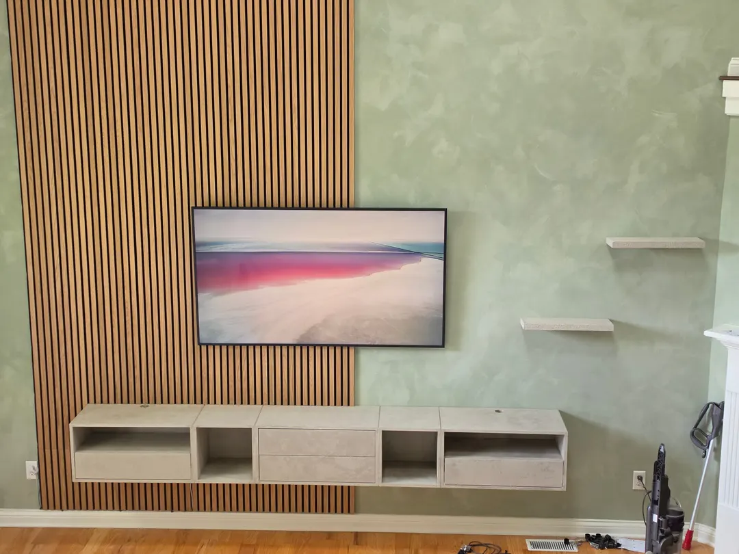 Floating cabinets and shelves plastered in a gray stone texture against a gray-green limewash wall and oak acoustic panels, in a Geist living room