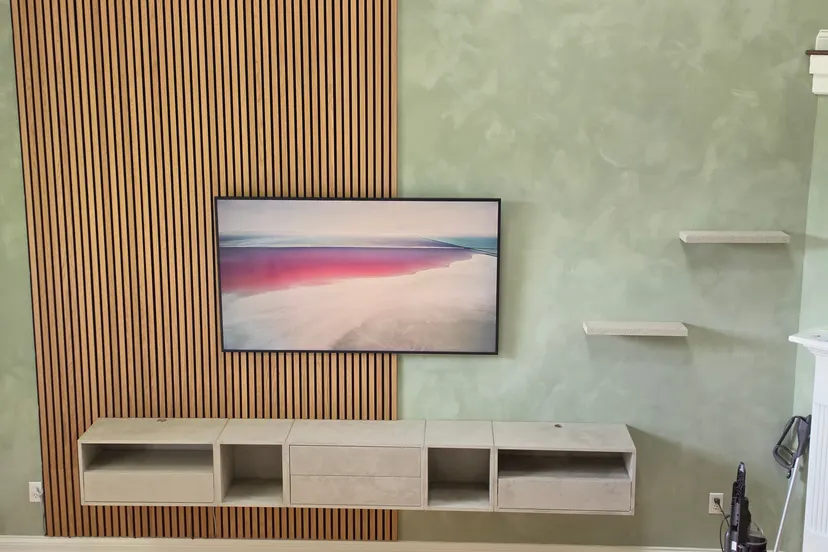 Floating cabinets and shelves plastered in a gray stone texture against a gray-green limewash wall and oak acoustic panels, in a Geist living room