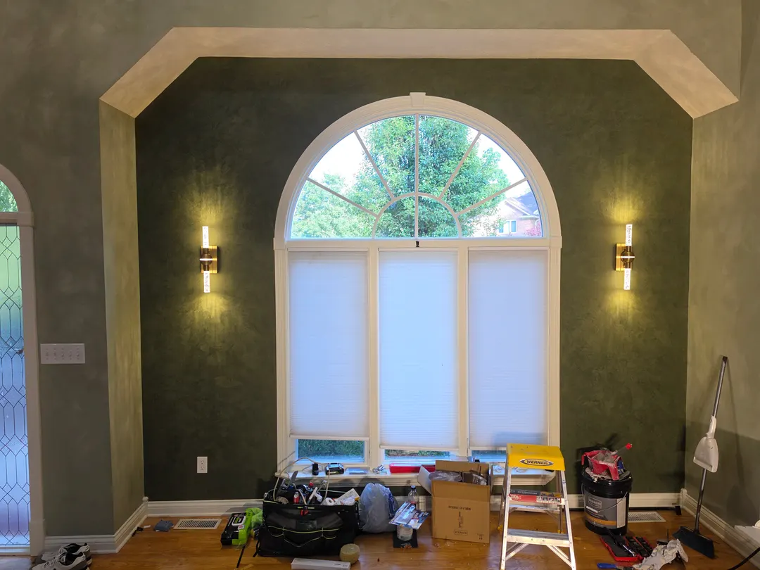 The inset wall in smoky green Roman clay around an arched window, with a sconce on each side