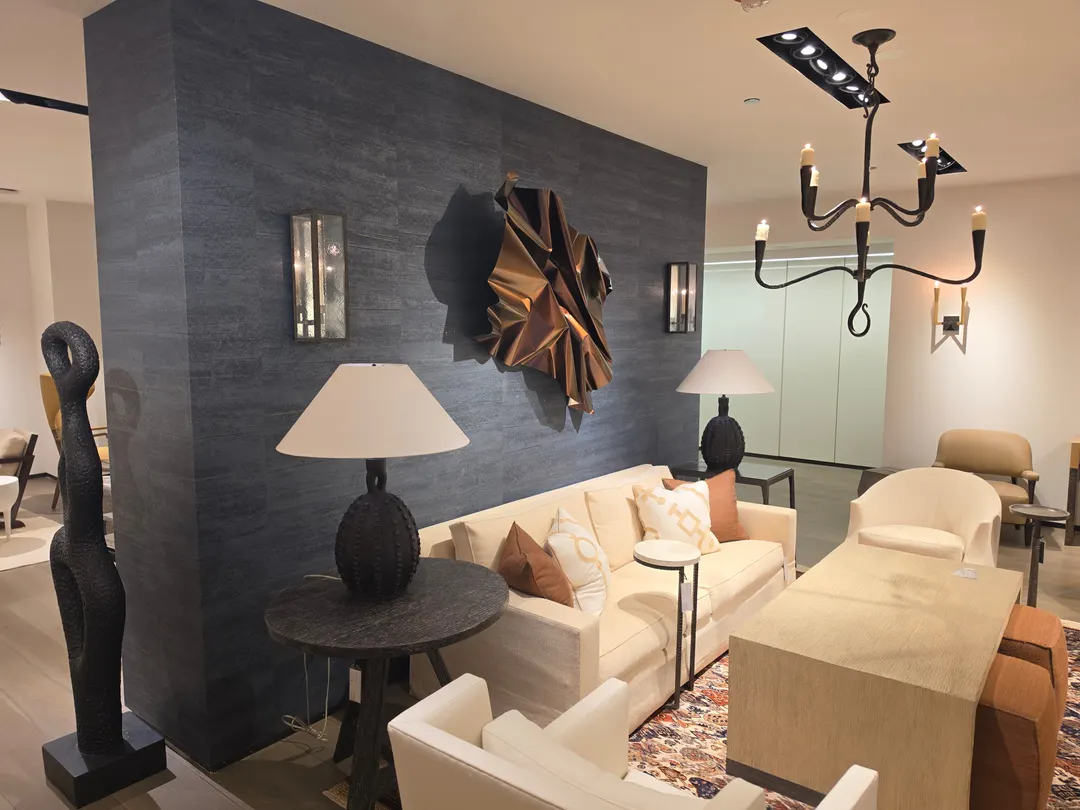 A tall freestanding wall in charcoal slate-look plaster, hung with lanterns and a copper-colored sculpture, behind a cream sofa and lamps in a large furnished room