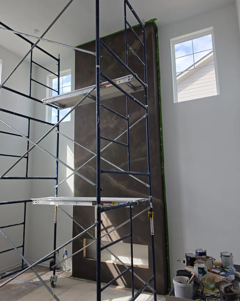 The espresso limewash column behind rolling scaffolding that reaches the ceiling