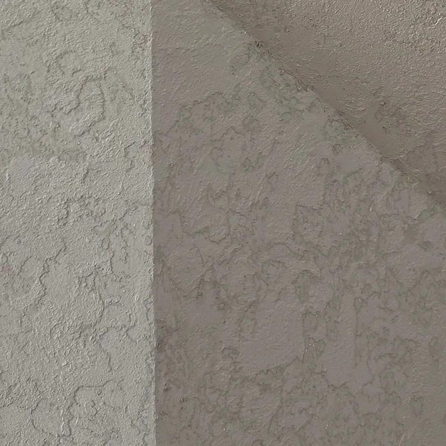 Close view of warm gray, stone-textured lime plaster turning a corner of a fireplace, in low light