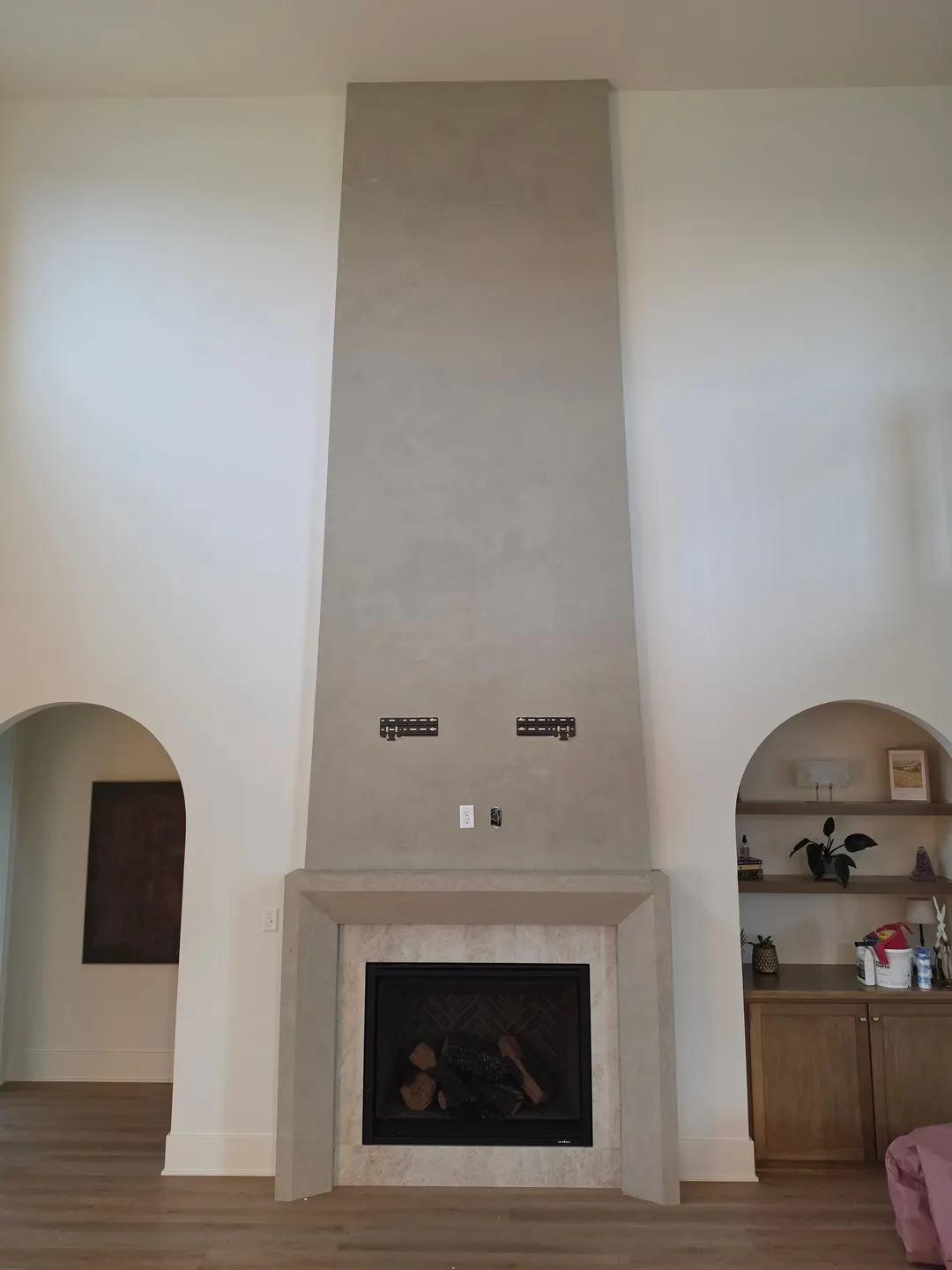 Tall, tapered warm gray column above the mantel, with the TV brackets in place, between two arched niches