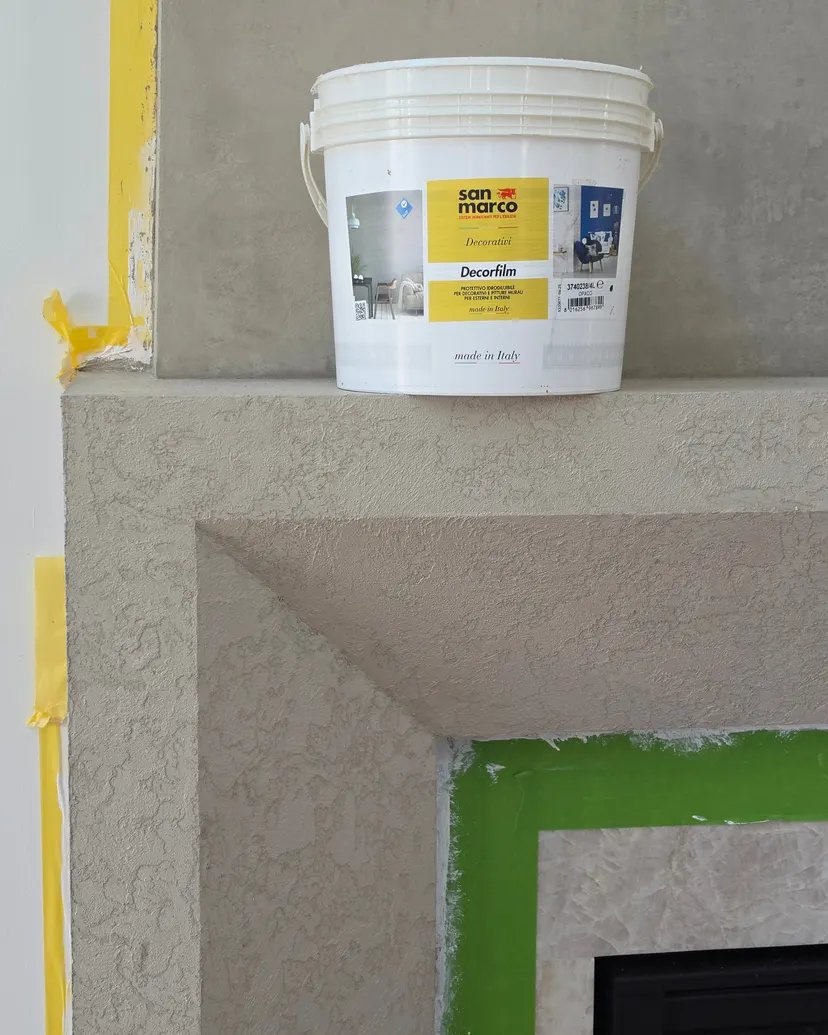 A corner of the mantel in warm gray lime plaster texture, with a product bucket on top and tape still around the firebox