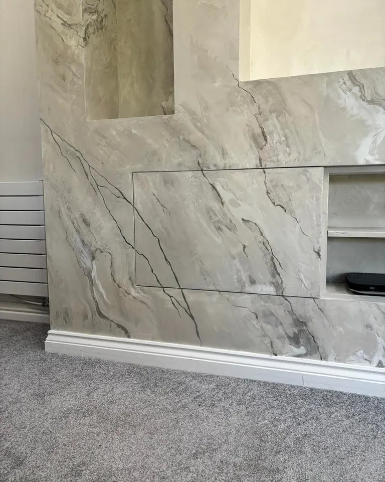 A media wall in gray-beige faux marble plaster with dark veins, open niches, and an inset panel, in a home