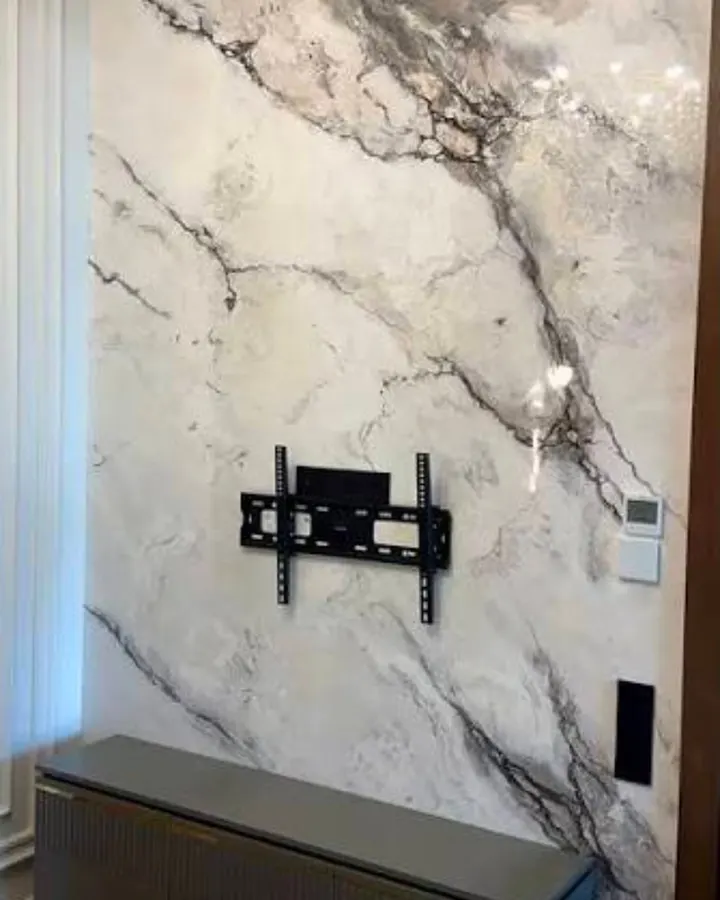 A high-gloss white marble-look plaster wall with sweeping gray veins, a TV mount, and a low dark cabinet