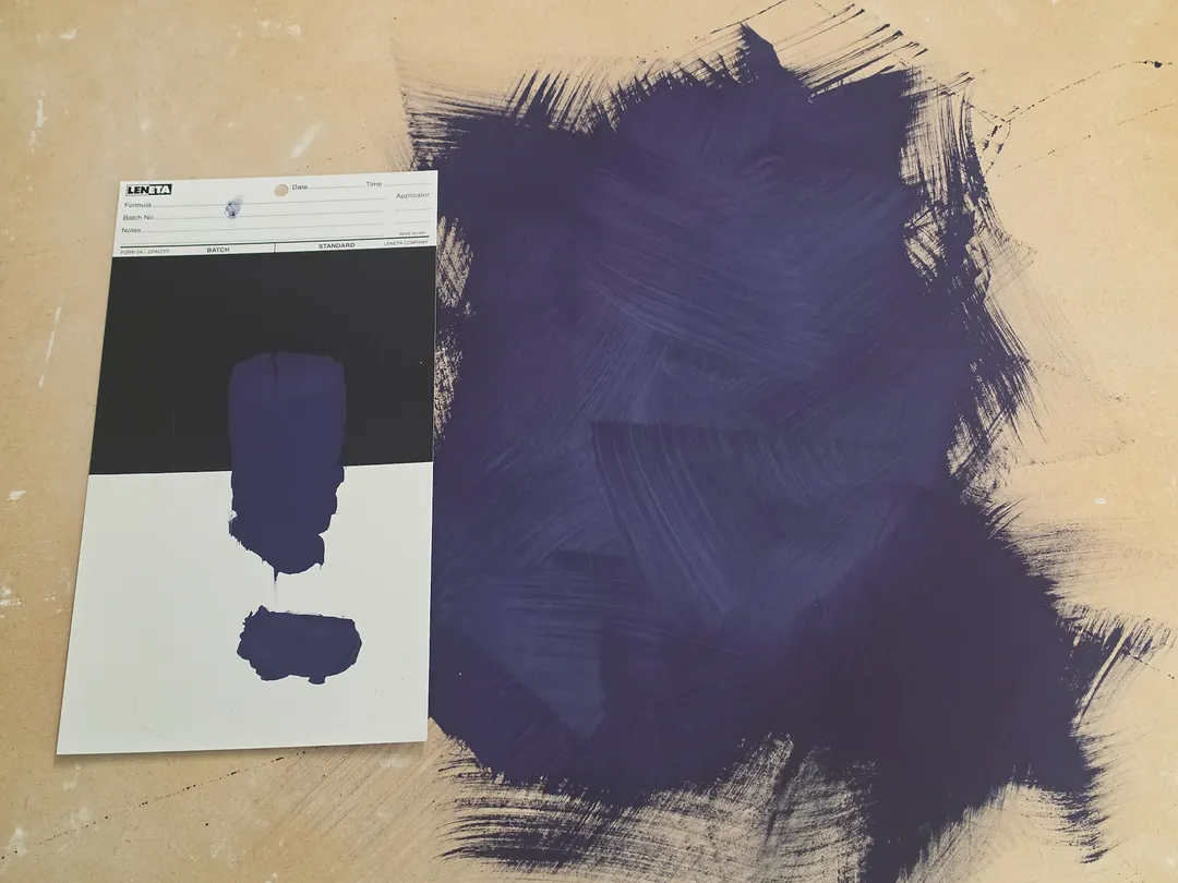 A deep violet-blue limewash brushed in crossing strokes across a board, beside a card with two swatches of the same color