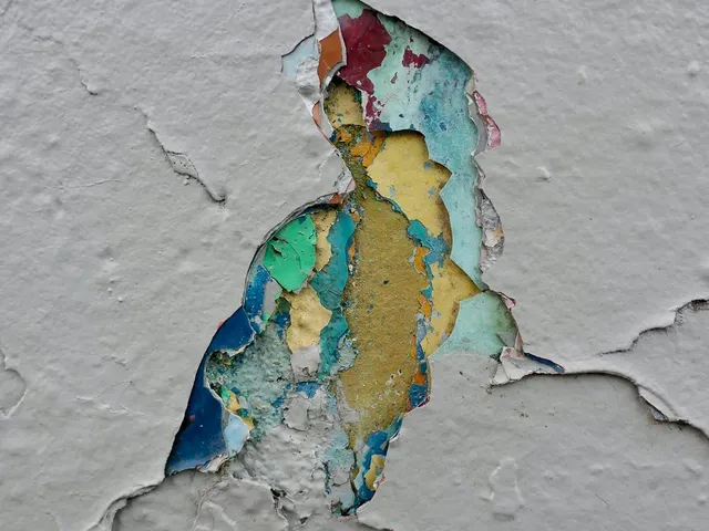 A chip in white paint revealing older layers of blue, yellow, and green