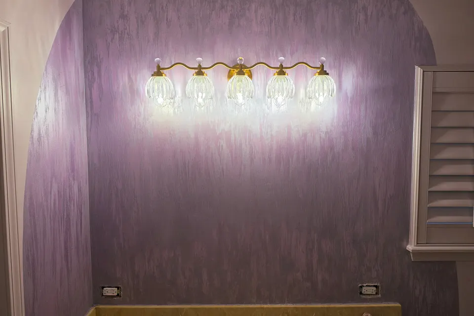 Lavender walls with pale streaks under a row of glowing glass vanity lights, in a Zionsville bathroom