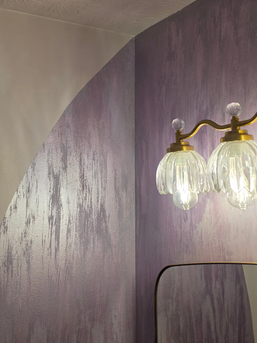 The lavender finish curving around the arched wall, beside the glass and brass vanity lights