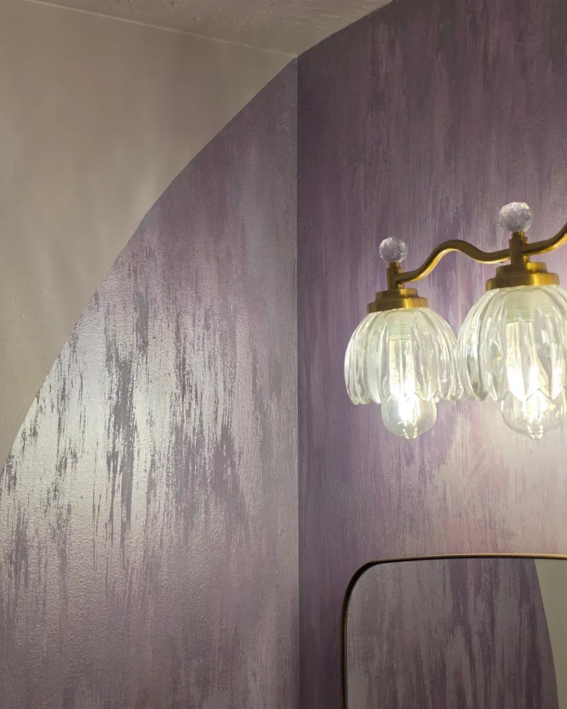 The lavender finish curving around the arched wall, beside the glass and brass vanity lights