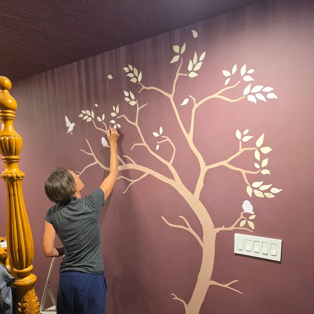 A member of our team painting the pale tree’s branches onto the oxblood wall beside the bed