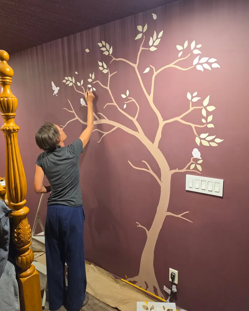 A member of our team painting the pale tree’s branches onto the oxblood wall beside the bed