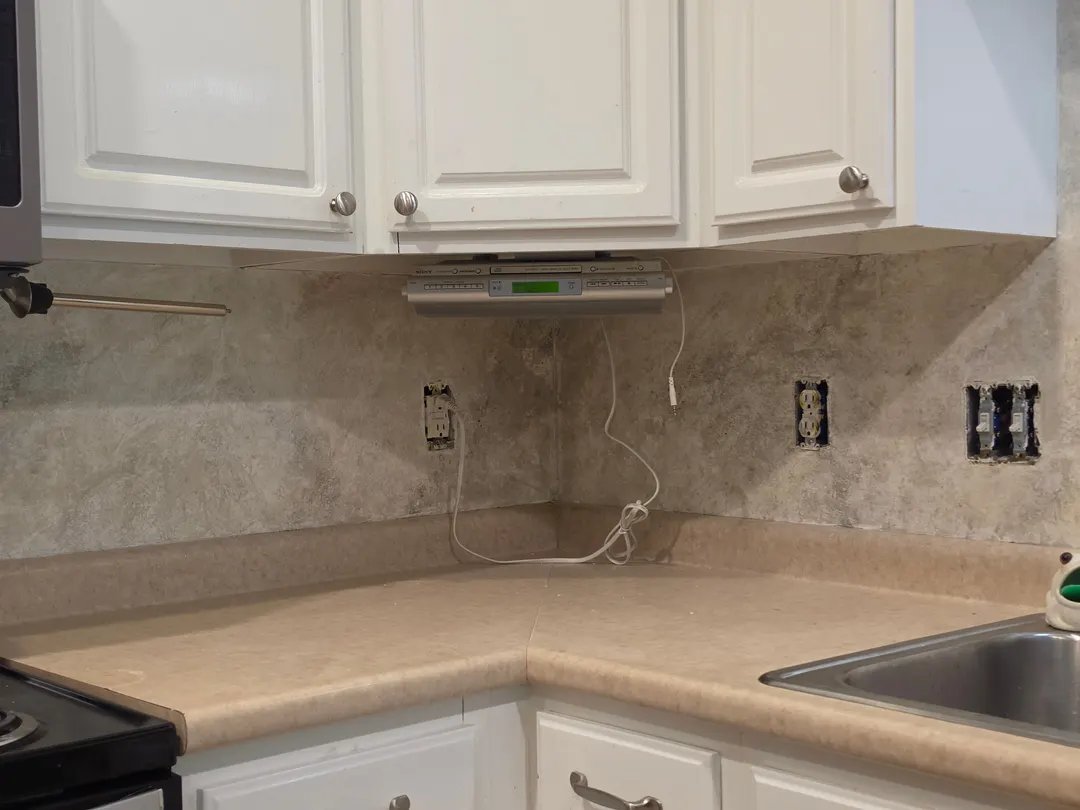The textured limestone backsplash turning a corner across two walls, under white cabinets